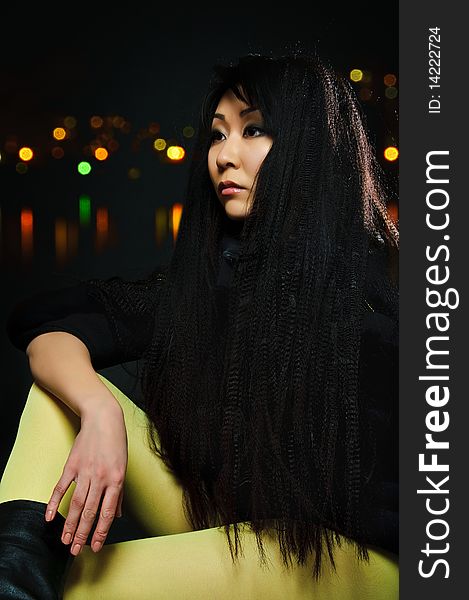 Sitting brunette asian model on black background with night light reflections