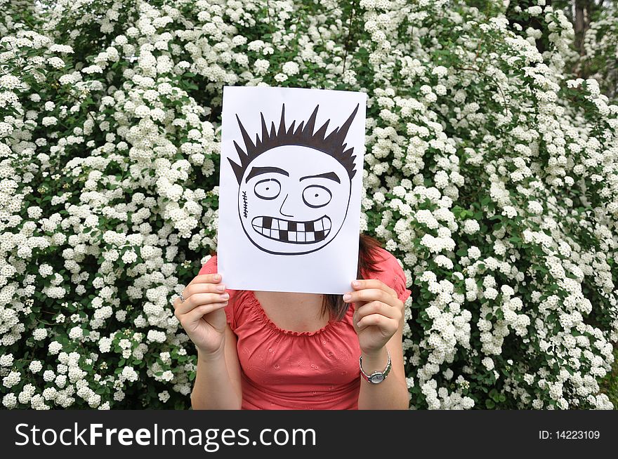 Beautiful girl holding a paper with a drawn face e