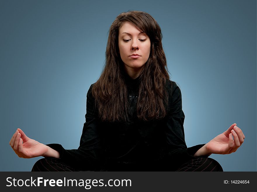 Attractive girl in dark clothes meditating, blue background