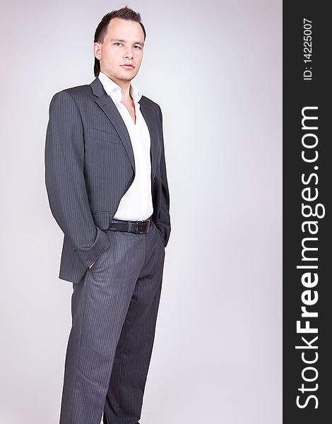 Young businessman standing, grey background.