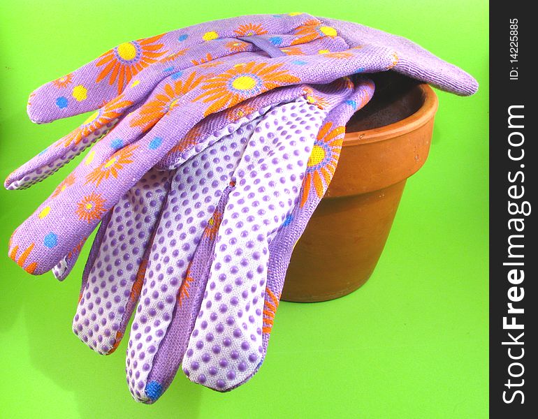 A flower pot with gardening gloves on a green background. A flower pot with gardening gloves on a green background