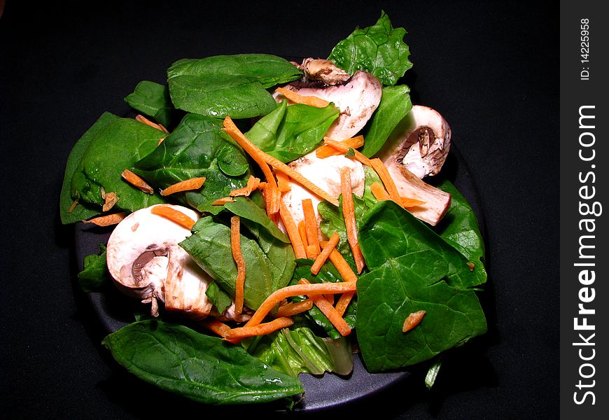 A fresh spinach, mushroom, carrot salad on black background. A fresh spinach, mushroom, carrot salad on black background