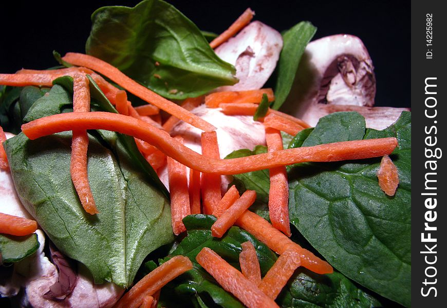 A fresh spinach, mushroom, carrot salad on black background. A fresh spinach, mushroom, carrot salad on black background