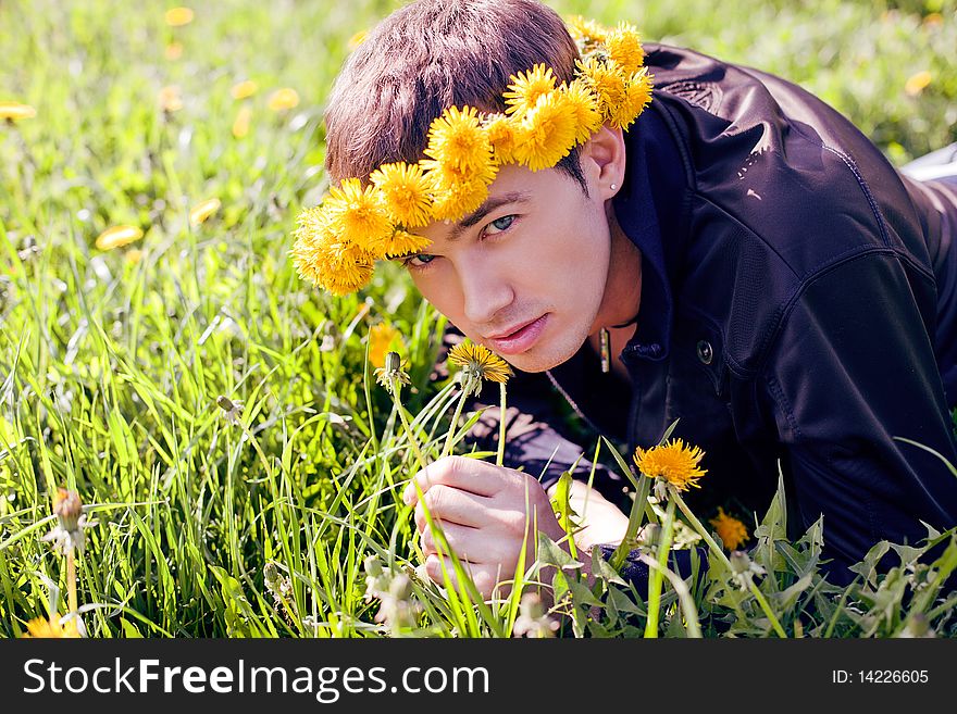 Young man in a clearing in the summer in a wreath of dandelions on the head