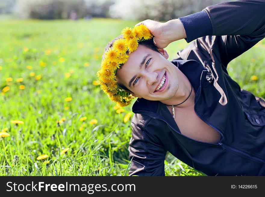 Young man in a clearing in the summer in a wreath of dandelions on the head