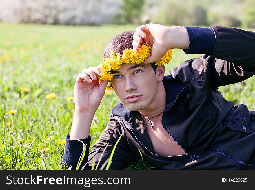 Young man in a clearing in the summer in a wreath of dandelions on the head