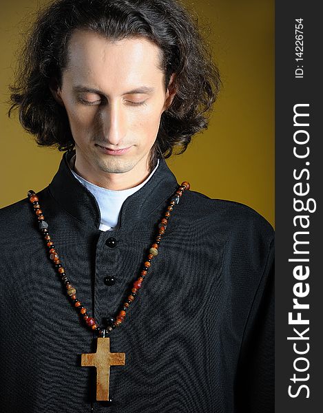 Conceptual portrait of Praying priest with wooden cross praying. yellow background