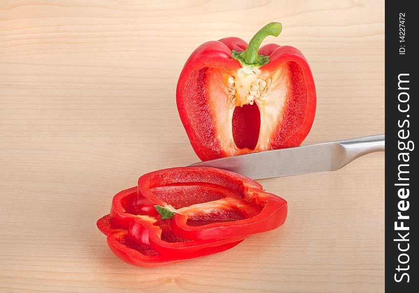 Red bell pepper sliced with a knife on a cutting board