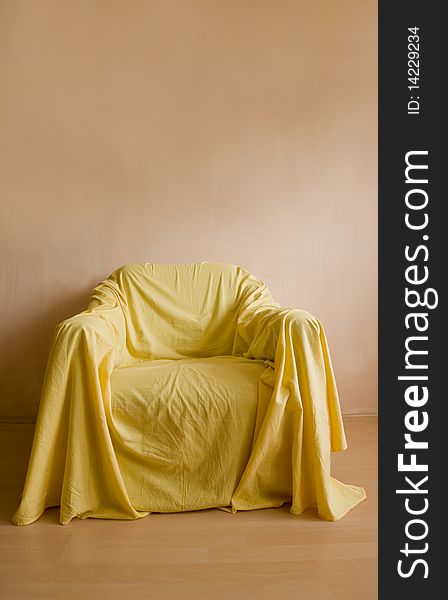 Armchair with yellow bed sheet on a wooden floor