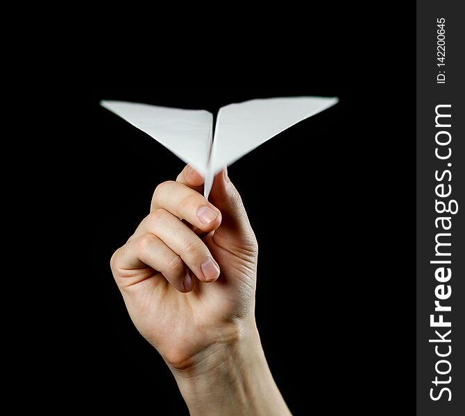 Hand holding a white paper airplane. Close up. Isolated on black background