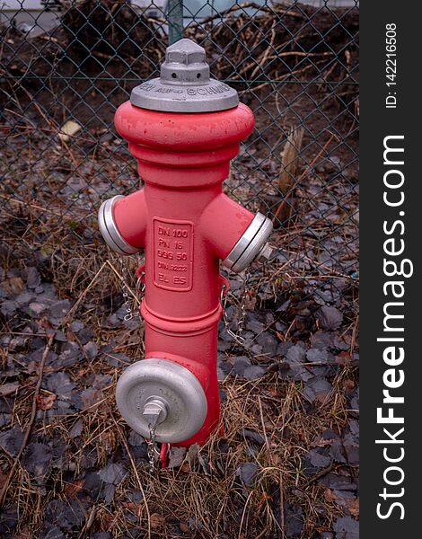 A red hydrant stands in front of a fence