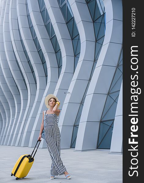 Beautiful young stylish Caucasian woman at the airport with a yellow suitcase and a straw hat goes on a journey. Beautiful young stylish Caucasian woman at the airport with a yellow suitcase and a straw hat goes on a journey.