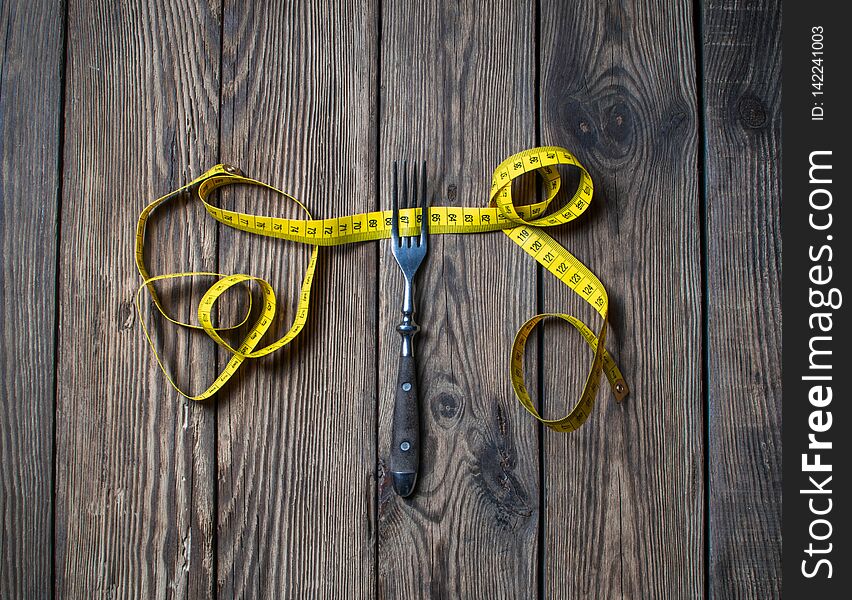 Diet concept, fork and measuring tape on wooden background. Fork and measuring tape on wooden background for a healthy lifestyle