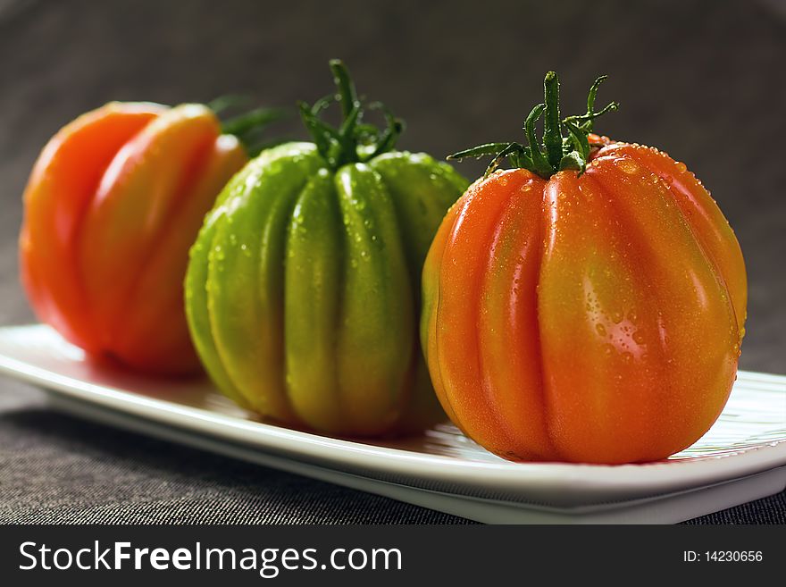 Three Red And Green Tomatoes On Grey Background. Three Red And Green Tomatoes On Grey Background