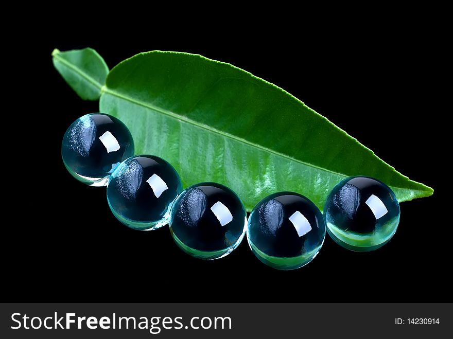 Close-up of green leaf and glass balls on a black background