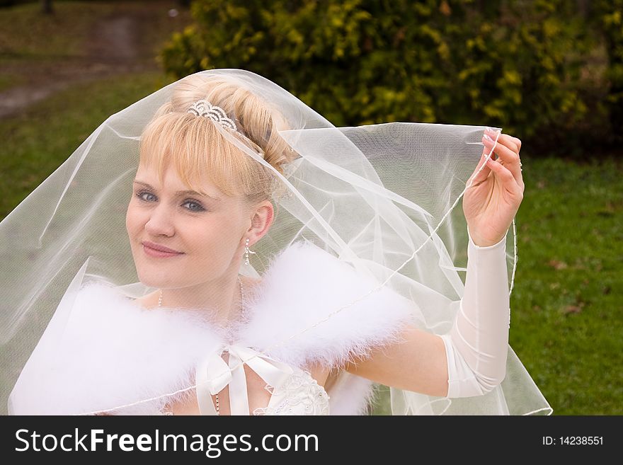 Beautiful bride is raising wedding veil. Newlywed is looking at the camera in outside.