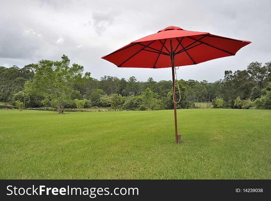 A large red unbrella on a patch of freshly mown green grass on a cloudy day. A large red unbrella on a patch of freshly mown green grass on a cloudy day