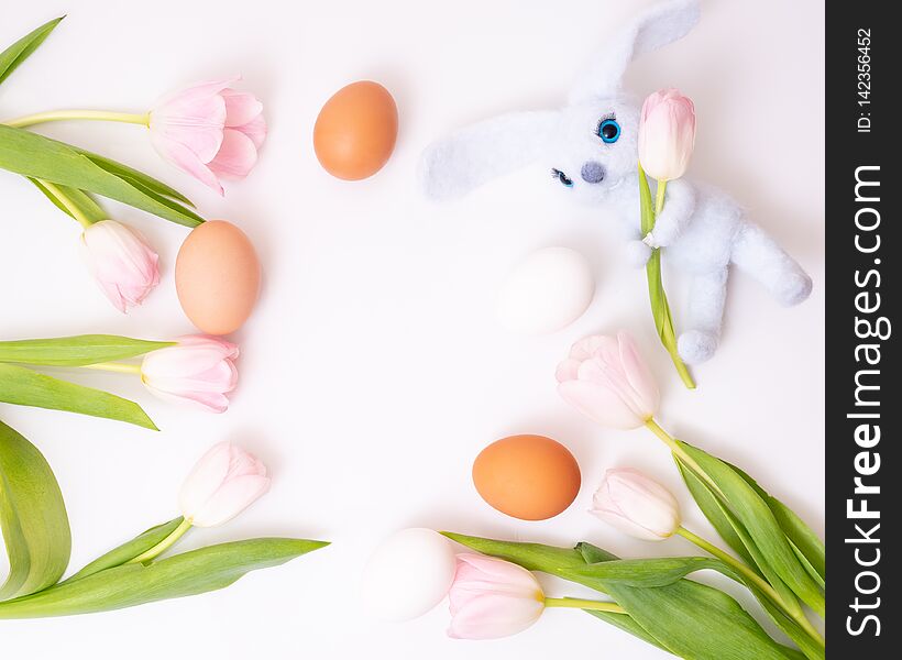 Blue toy rabbit three colored eggs mixed with pink tulips. Top view.