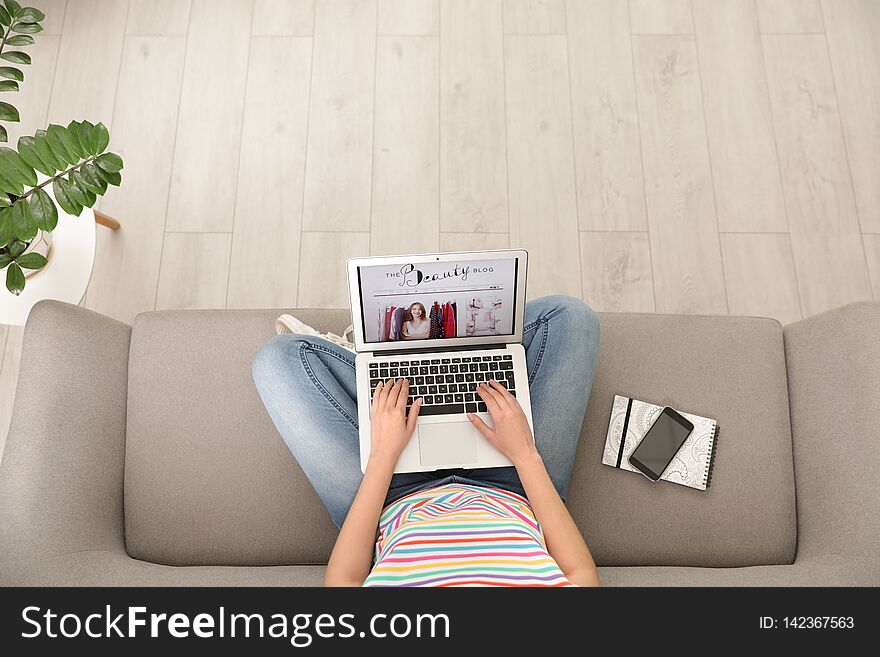 Woman holding laptop with open beauty blogger site on sofa