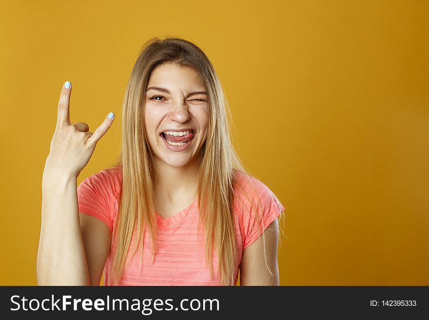 Beauty portrait of young fresh looking blonde woman with devil gesture over yellow background. Beauty portrait of young fresh looking blonde woman with devil gesture over yellow background