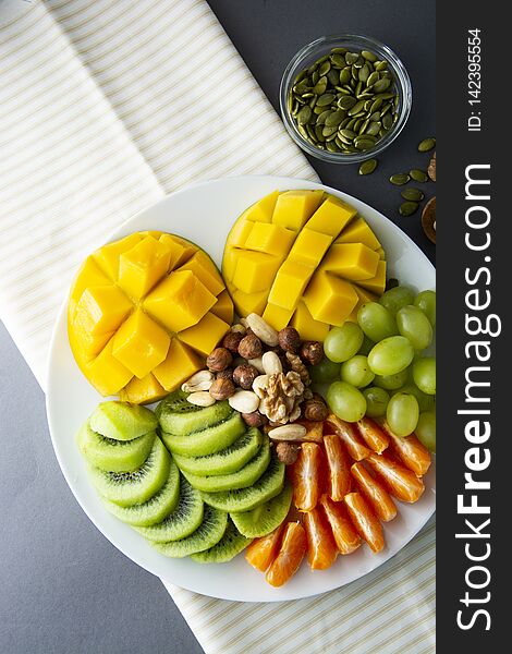 Delicious fruits platte isolated. Mango, kiwi, citrus, nuts, grapes. Mix of various exotic fruits. Healthy fruit salad, healthy