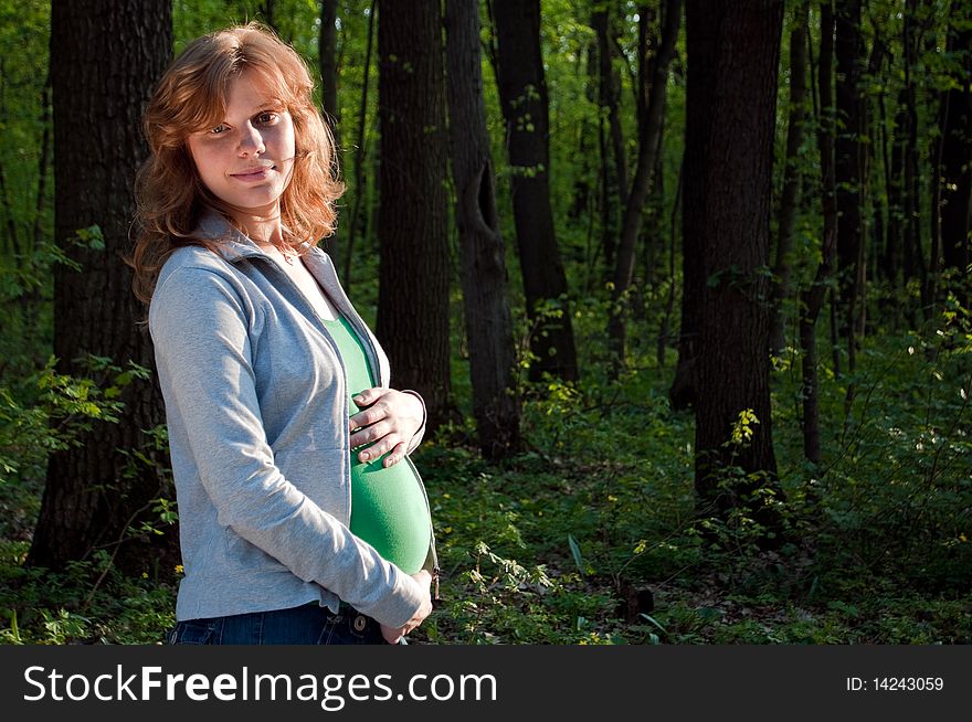 Happy young pregnant woman holding her hands on her tummy