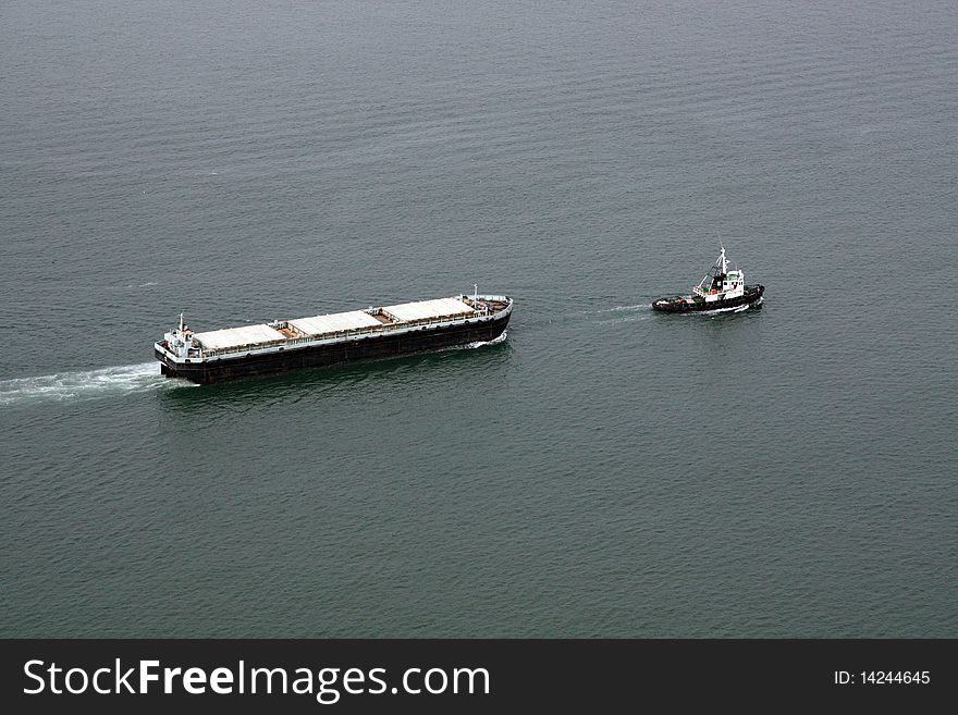 Aerial view of a cargo transportation ship escorted by a small fishing boat. Aerial view of a cargo transportation ship escorted by a small fishing boat.