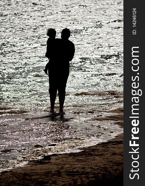 View of a mother holding a child on the shore of the beach. View of a mother holding a child on the shore of the beach.