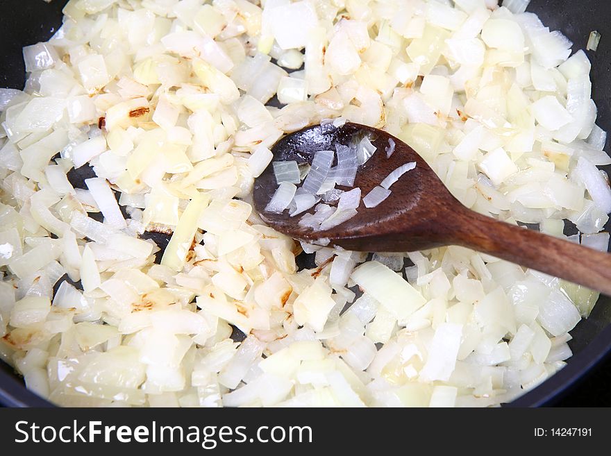 Onion being fried on a pan with a ladle