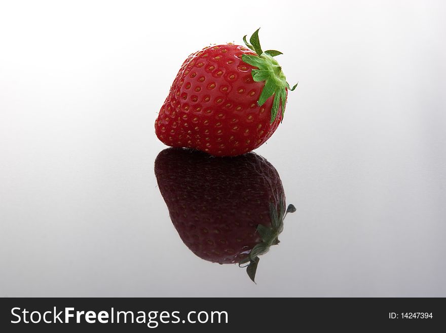 Single ripe fresh strawberry on dark reflecting surface