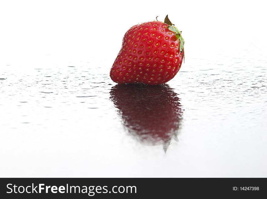 Single ripe fresh strawberry on wet dark reflecting surface with water drops