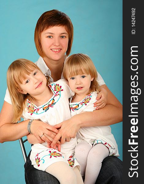 Young happy mother with two small daughters on blue background. Young happy mother with two small daughters on blue background