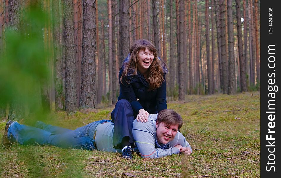 Portrait of a cheerful laughing couple - he is lying on a grass and she is sitting on his back. Portrait of a cheerful laughing couple - he is lying on a grass and she is sitting on his back