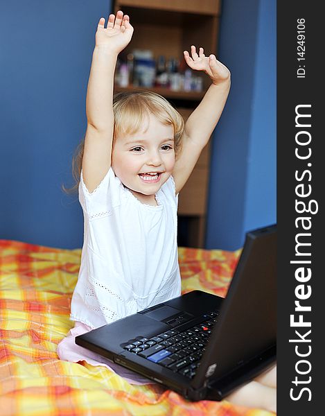Cheerful little girl with laptop sits on bed of parents