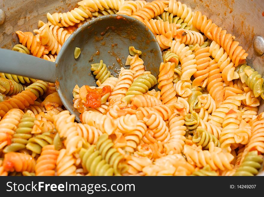 A big pot of pasta covered with tomato sauce with ladle