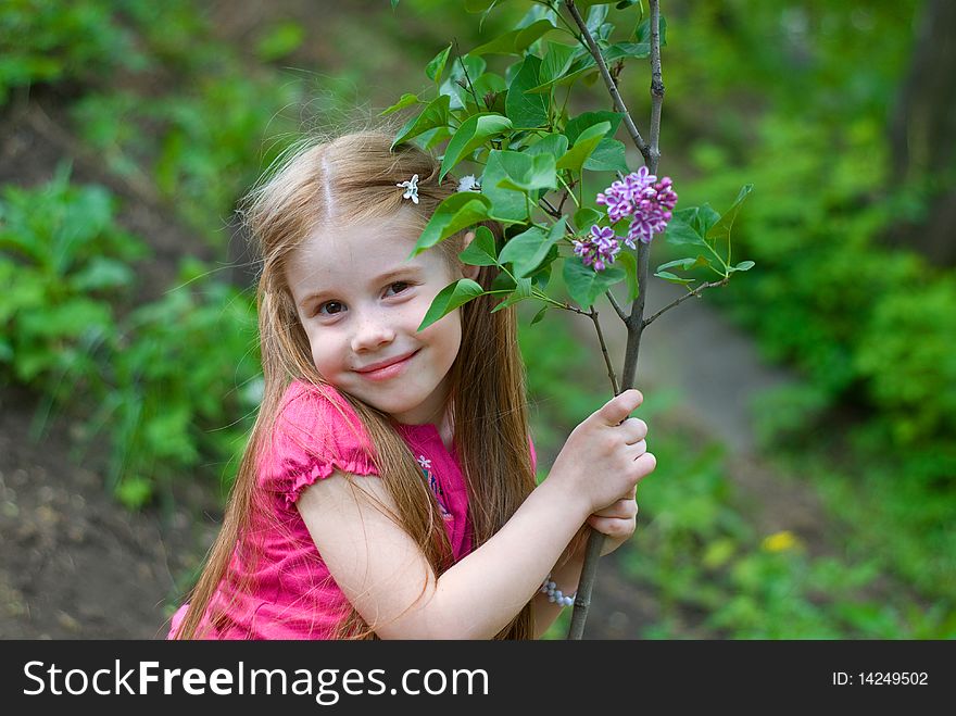 Smiling nice little girl holding lilacs at the trunk