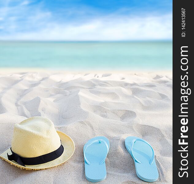 Beach summer holiday background. Flip flops and hat on sand near ocean. Summertime accessories on seaside. Tropical vacation and relax travel concept. Top view and copy space. Selective focus