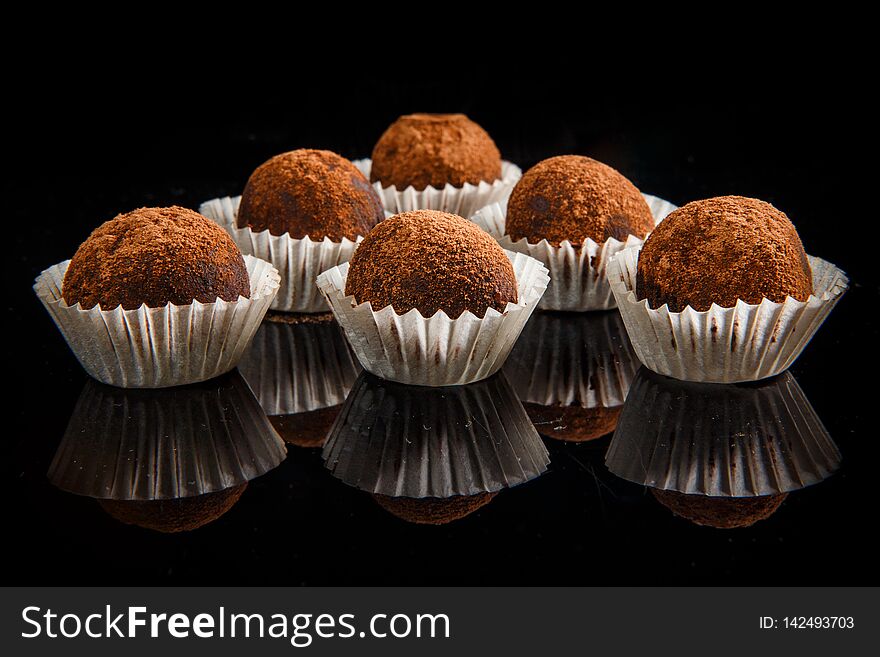 Big group of healthy useful organic handmade round chocolate candies decorated with brown cocao powder on black mirror background. Big group of healthy useful organic handmade round chocolate candies decorated with brown cocao powder on black mirror background