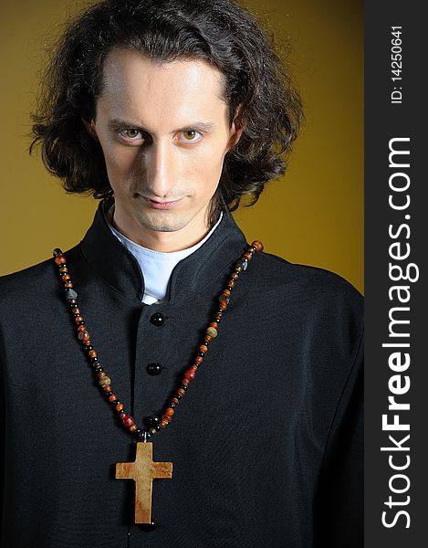 Conceptual portrait of Praying priest with wooden cross praying. yellow background