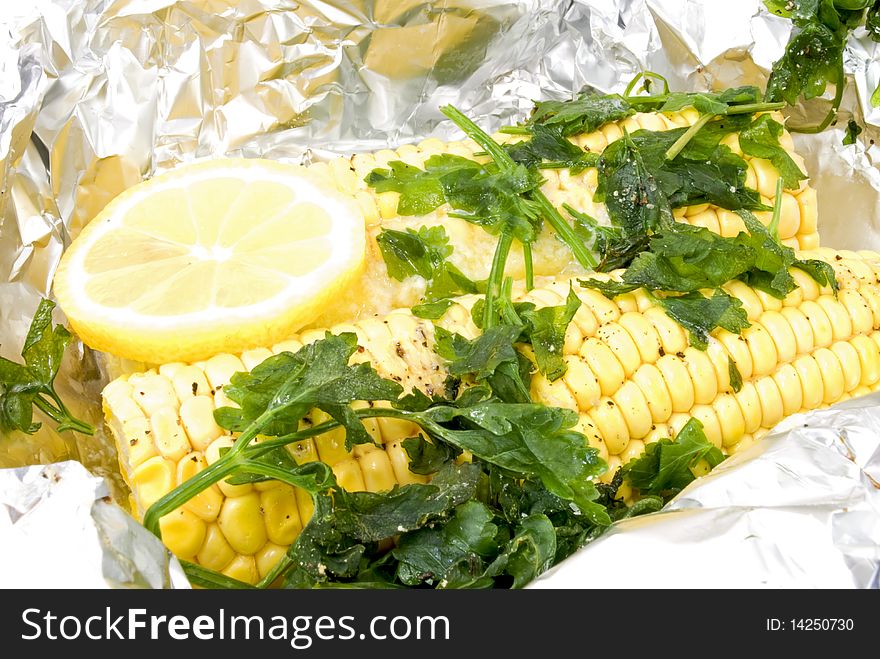 In aluminium foil steamed corn cobs decorated with parsley and lemon
