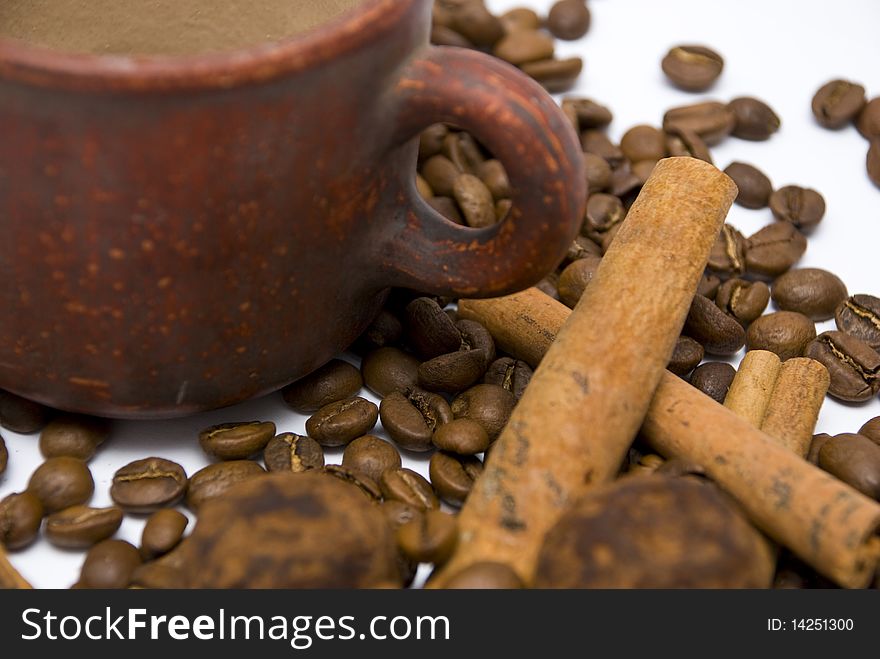 Ceramic cup red, fragrant coffee beans, sweets chocolate truffles and cinnamon sticks on a white background close-up. Ceramic cup red, fragrant coffee beans, sweets chocolate truffles and cinnamon sticks on a white background close-up