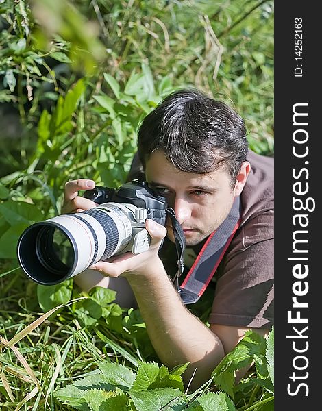 Young male bird watcher laying down holding photo camera with tele lenses. Young male bird watcher laying down holding photo camera with tele lenses