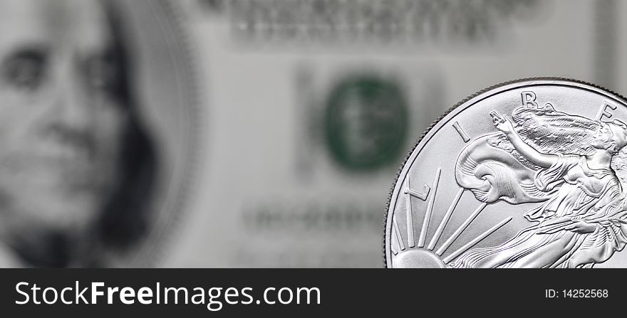 Silver shiny dollar coin on a background of blurry one hundred dollar bill. Silver shiny dollar coin on a background of blurry one hundred dollar bill