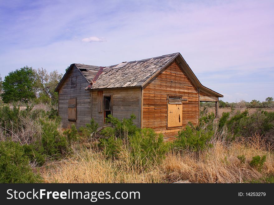 An old derelict wooden house with peeling tiles and broken and boarded windows in the semi-desert of Utah USA. An old derelict wooden house with peeling tiles and broken and boarded windows in the semi-desert of Utah USA.