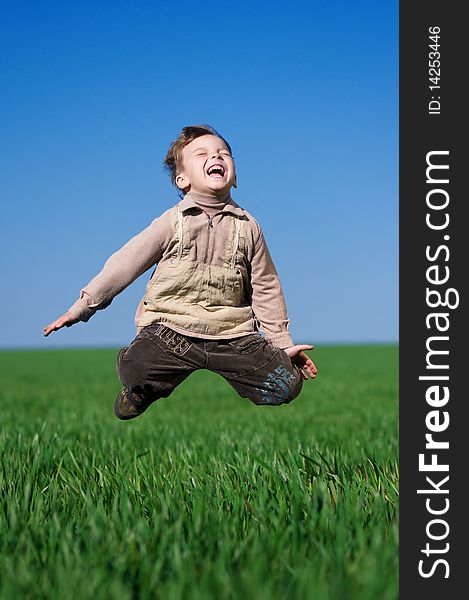 Happy little boy jumping in field against blue sky. Happy little boy jumping in field against blue sky