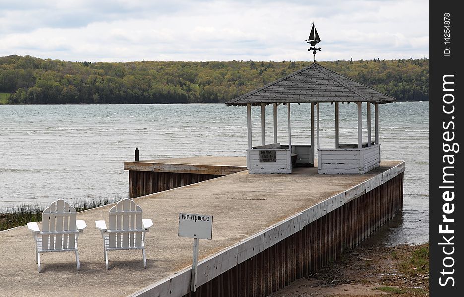 An old weathered private empty dock on Lake Michigan with two chairs and gazebo showing a peaceful scene overlooking the water. An old weathered private empty dock on Lake Michigan with two chairs and gazebo showing a peaceful scene overlooking the water.