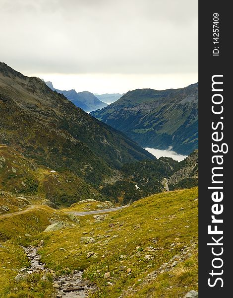 A small road called the Suestenpass travels through the Swiss alps towards a fog-filled valley below. A small road called the Suestenpass travels through the Swiss alps towards a fog-filled valley below.