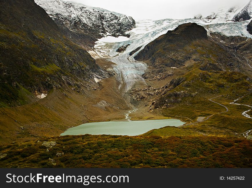 A glacier comes over the top of a mountain and a stream coming off of it runs into a small lake near the Suestenpass in the Swiss alps. A glacier comes over the top of a mountain and a stream coming off of it runs into a small lake near the Suestenpass in the Swiss alps