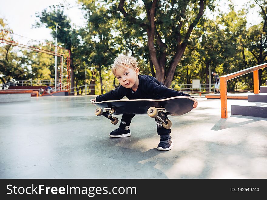Little boy carries a skateboard outside in the park. Little boy picks up a skateboard. Little boy carries a skateboard outside in the park. Little boy picks up a skateboard