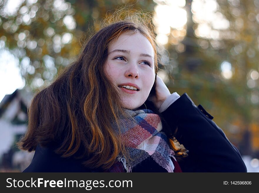 A beautiful girl with reddish hair smiles and removes a long strand of hair over her shoulder, being in the Park in the cold season
